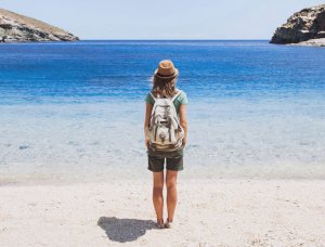 Frau steht mit Rucksack am Strand