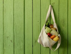Stofftasche befüllt mit Gemüse hängt an grüner Wand, einkaufen mit Stofftasche, um Müll zu vermeiden